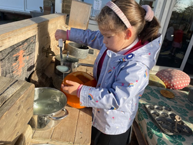 Reception child filling a pumpkin with water for Harvest Festival